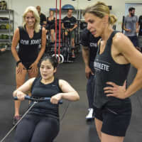 <p>Anyssa Lucena, right, encourages Gym Jones athletes to dig deep on the rowing machine.</p>