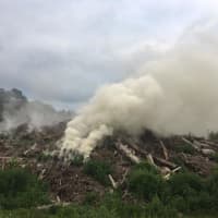 <p>A smoky fire burns at a mulch pile Tuesday on Button Shop Road in Newtown. Crews from Botsford Fire Rescue are on the scene.</p>