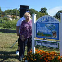 <p>Kaye Backer, mother of the late Terry Backer, poses with the sign naming Stratford&#x27;s Community Garden after her son.</p>