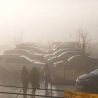 <p>Shoppers navigate a foggy parking lot as fog, rain and warm temperatures envelop the area.</p>