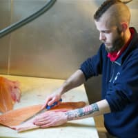 <p>Assistant Manager Zachary Redin cuts up a salmon.</p>