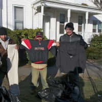 <p>Four men hold up coats and clothing items they received at the mission.</p>