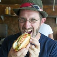 <p>Noshi&#x27;s owner Peter Newman takes a bite out of one of his trademark hot dogs.</p>