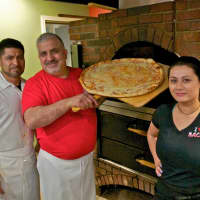 <p>Chef Gerardo Carino (center) pulls a pizza from the brick oven at Pizzeria Bacio.</p>