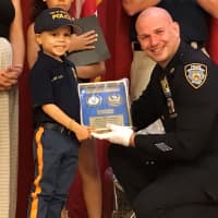 <p>NYPD Detective Damian Majersky and Alex Hammer hold a plaque displaying Alex&#x27;s honorary detective shield.</p>