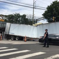 <p>A Stamford police officer directs traffic around a wrecked tractor-trailer that tried and failed to negotiate a railroad underpass on East Main Street in Stamford.</p>
