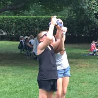 <p>Two girls use a pair of protective solar glasses to try to take a photo of the eclipse on Monday in Ballard Park.</p>