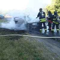 <p>Westport firefighters douse a car fully engulfed in flames on Saturday evening on the Merritt Parkway.</p>