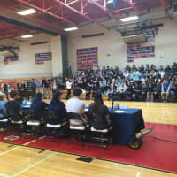 <p>Friends, family and other students sit in bleachers across a gym as seven Byram Hills High School senior athletes sign letters of intent with colleges.</p>