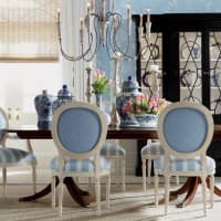 <p>In this dining room, the blue used on the chairs and walls perfectly complements the warm wood table. A dramatic black display cabinet nearby lends visual weight and a modern edge to the otherwise traditional furnishings.</p>