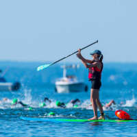<p>A woman on a paddleboard keeps an eye on the swimmers near the start of the event.</p>