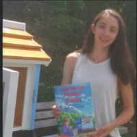 <p>14-year-old Juliette Castagna shows one of the books that is currently in the Little Free Library that she installed in Ridgefield.</p>