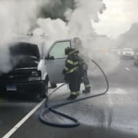 <p>Fire crews douse the inside of a burning cargo van during the Monday morning rush hour on the Merritt Parkway in Fairfield.</p>