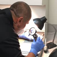 <p>Sgt. Alex Tolnay of the Norwalk cold case unit examines a phone for finger prints.</p>