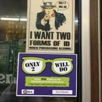 <p>Stickers requiring two forms of ID to purchase alcohol are displayed in a store window.</p>
