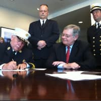 <p>Stamford Fire Department Chief Peter Brown signs an agreement consolidating services with Turn of River Volunteer Fire Department as Stamford Mayor David Martin, sitting, looks on. </p>