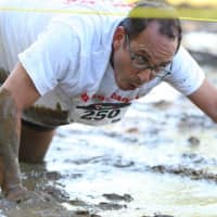 <p>A runner crawls through a muddy section of the course.</p>