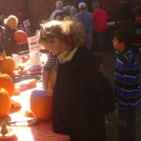 <p>Elissa Thompson (right) and other volunteers scoop innards out of pumpkins that families selected to get them ready for carving.</p>