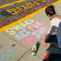 <p>Parent Brieana Kennedy draws &quot;smiles are fun to share,&quot; at Kings Highway Elementary School on Friday, Oct. 17, as a part of the Kindness in Chalk movement.</p>