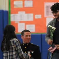 <p>A military veteran receives flowers and a flag from a student.</p>