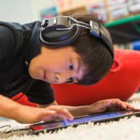 <p>A boy listens to headphones will working on a computer tablet during a Curiosity In Action camp last summer at Fairfield Country Day School.</p>