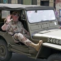<p>A veteran waves from a jeep.</p>