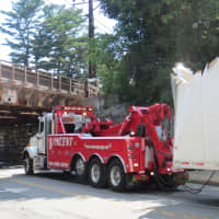 <p>A tow truck is hooked up to the trailer which struck a railroad overpass (to the left) in Rye on Monday.</p>
