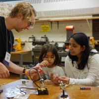 <p>Local business owner Travis Sluss of MacInspires teaches a mother and daughter how to solder electric circuits.</p>