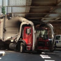 <p>A garbage truck is stuck under the Washington Street train bridge in Norwalk on Monday.</p>