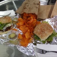 <p>A bag of greasy goodness -- aka sweet potato chips -- spill out of a bag between two of Poppy&#x27;s famous grass-fed beef burgers.</p>