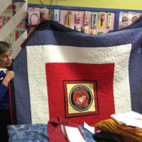 <p>Jane Dougherty, the Connecticut representative for Quilts of Valor, center, shows a quilt to be presented to a former Marine (left).</p>