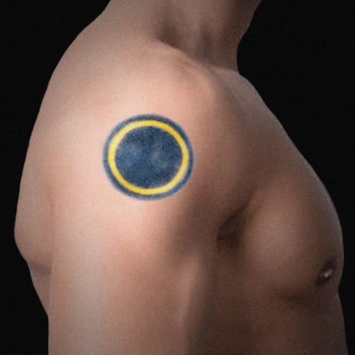 The body has a distinct tattoo on the right shoulder which resembles a solar eclipse.