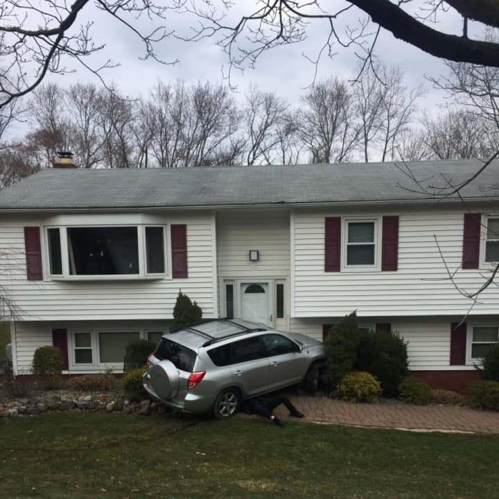 A tow truck driver works to remove a car from the front of the house it hit.