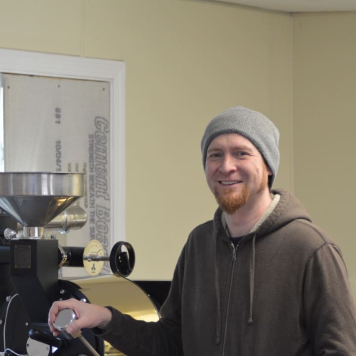 Sherman resident John Rich, owner of Sacred Grounds Coffee Roasters, poses in front of his coffee roaster Monday.
