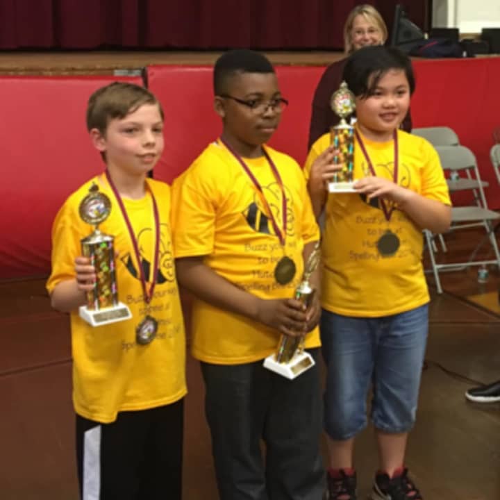 Principal Carla Tarazi proudly looks on at three spelling bee winners holding their trophies.