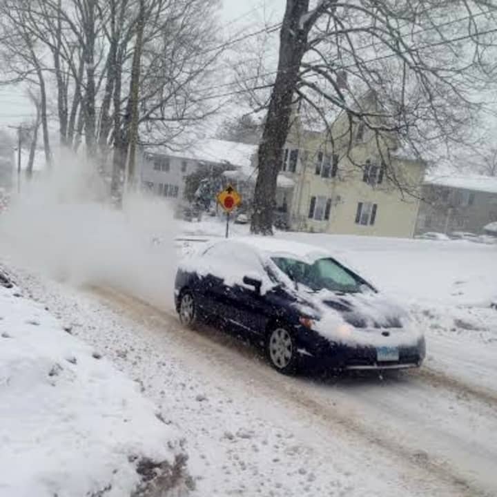 A car burns some rubber and kicks up some snow as it spins its wheels going up a steep hill in Danbury. 