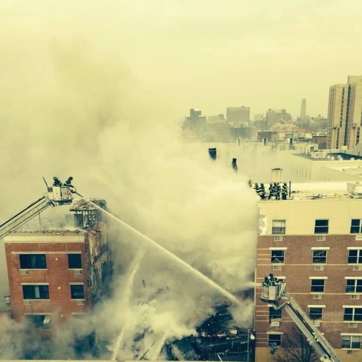 Fire crews are battling a blaze following a huge explosion that collapsed a building in Harlem and has suspended all Metro-North traffic in the city.