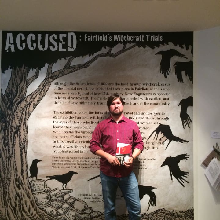 Graphic novelist Jakob Crane poses in front of the entrance to the &quot;Accused: Fairfield&#x27;s Witchcraft Trials&quot; exhibit. Crane is the artist behind the exhibit&#x27;s panels and murals.