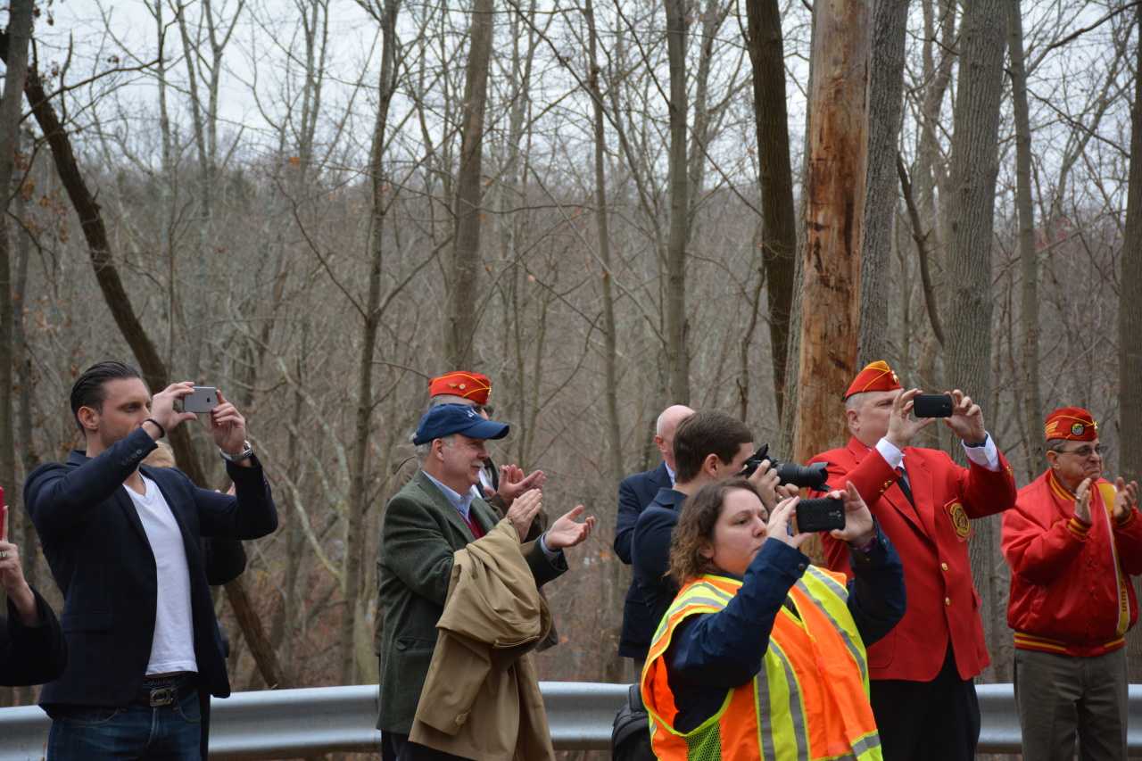 Onlookers hold phone cameras out during the unveiling of signage along Route 137 in Pound Ridge that is in honor of Eric Jones.