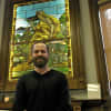 Glass restorer Michael Skrtic, of The Glass Source in Shelton, stands in front of one of the panels he restored at the Plumb Library.
