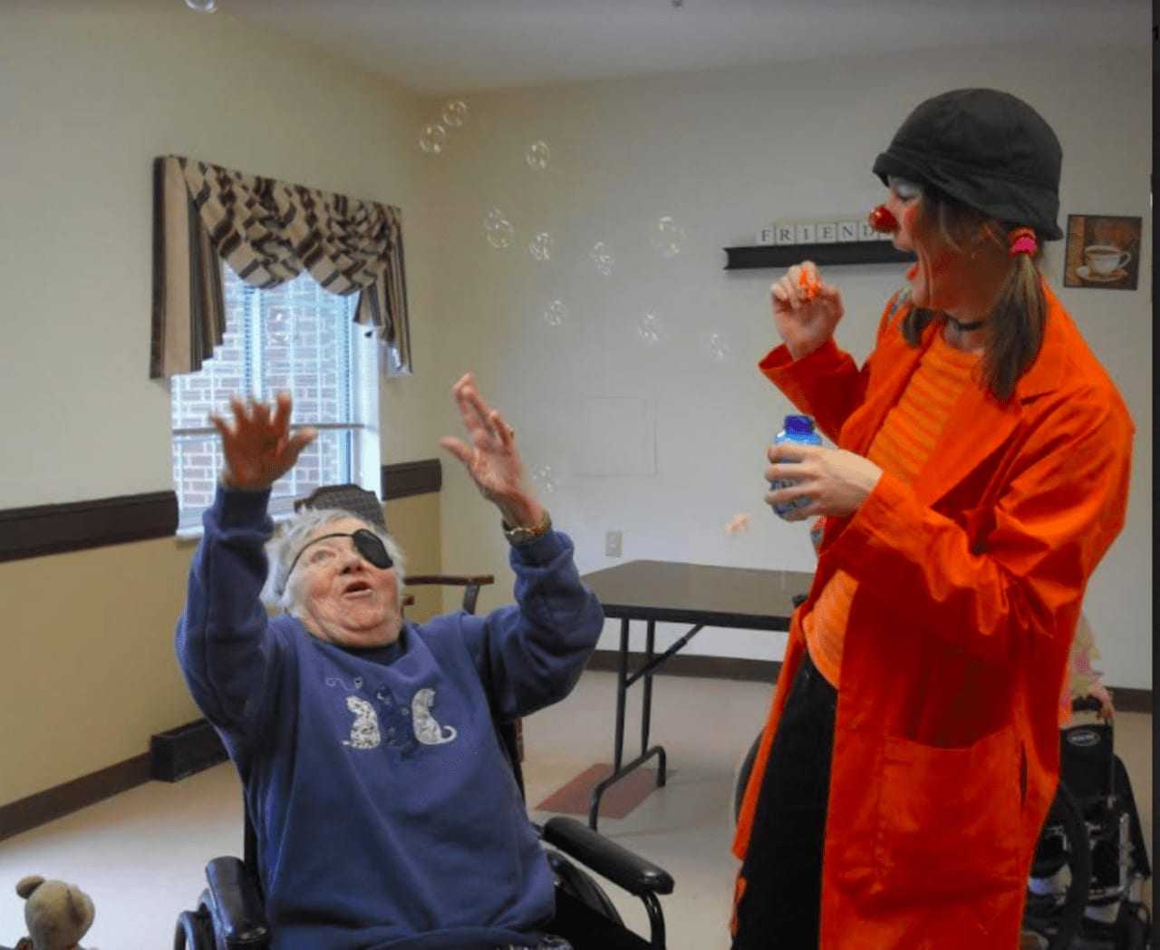 Spark Arts owner, Cynthia Rauschert, dressed as a clown, working with seniors.