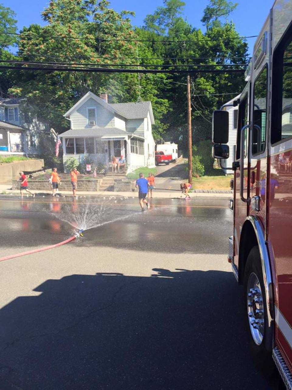 Runners cool off by trotting through a spray set up by Bethel's fire and emergency services departments Monday.