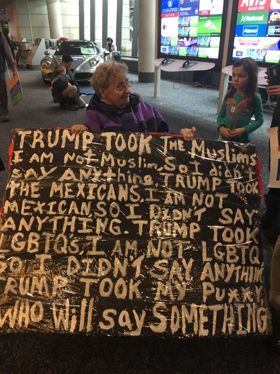 A protester who identified herself only as Shirley joins the crowd at Bradley Airport with her sign propped on her walker. She is 93 and from West Hartford.