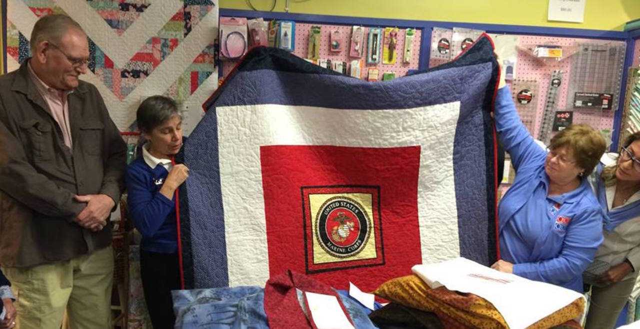 Jane Dougherty, the Connecticut representative for Quilts of Valor, center, shows a quilt to be presented to a former Marine (left).