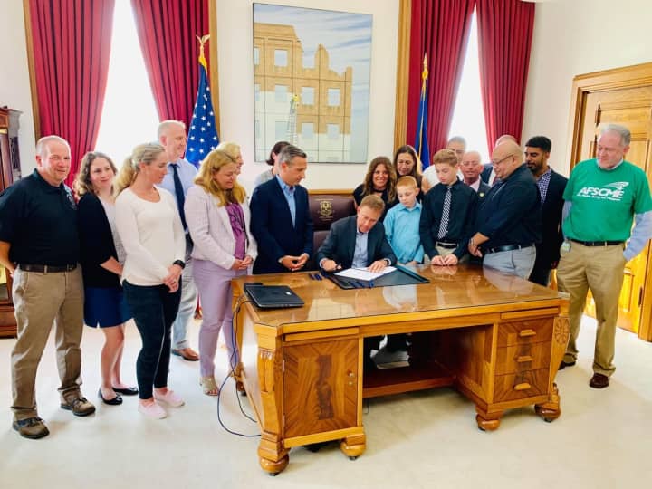 Norwalk police officer Phil Roselle and his family watch Gov. Ned Lamont sign &quot;Phil&#x27;s Bill&quot; into law allowing Connecticut municipalities to give full pensions to injured officers. His wife Debbie Roselle fought for and applauds the legislation.