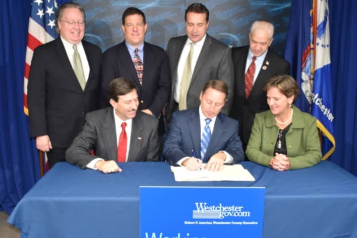 Westchester County Executive Robert P. Astorino signs the $1.8 billion budget on Friday, Dec. 18, as members of the budget coalition look on.