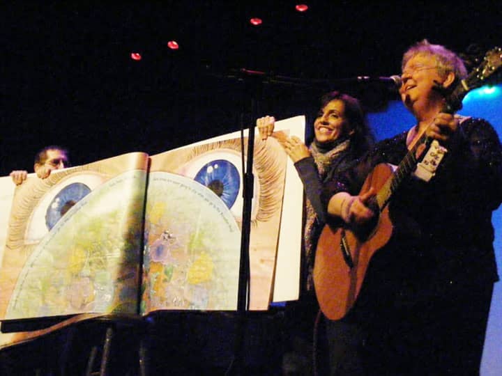 Piermont&#x27;s Betsy Franco Feeney and another audience member hold the giant copy of the children&#x27;s book “Amoeba Hop” at Hurdy Gurdy’s in Fair Lawn, N.J. while folksinger Christine Lavin plays.