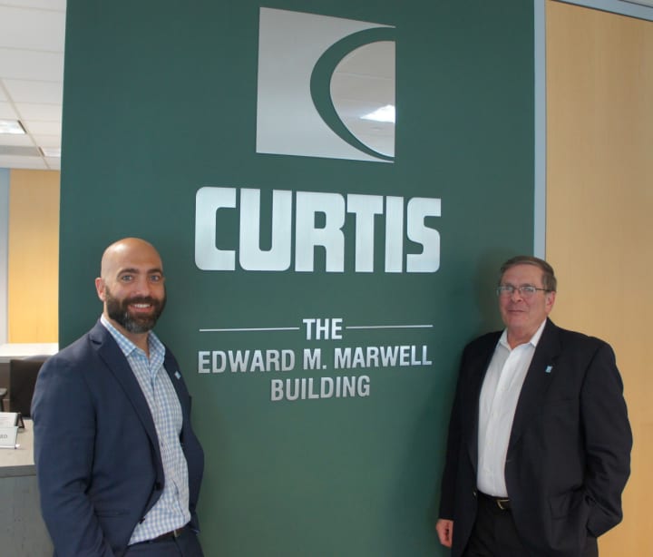 Nick Marwell, left, and his father Stuart Marwell, right, stand in front of the Curtis dedication to company founder Edward M. Marwell.