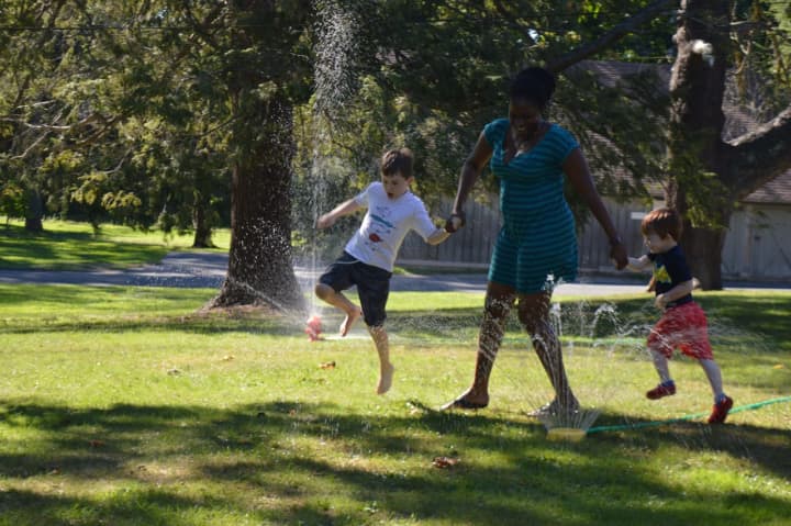 Maddox Bragg, his babysitter Stacy-Ann Hercules and his little brother, Lincoln, frolic in the sprinklers at the Pequot Water Games in Fairfield.