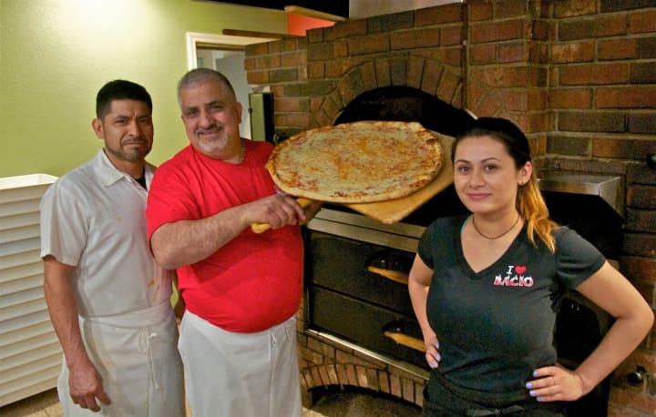 Chef Gerardo Carino (center) pulls a pizza from the brick oven at Pizzeria Bacio.